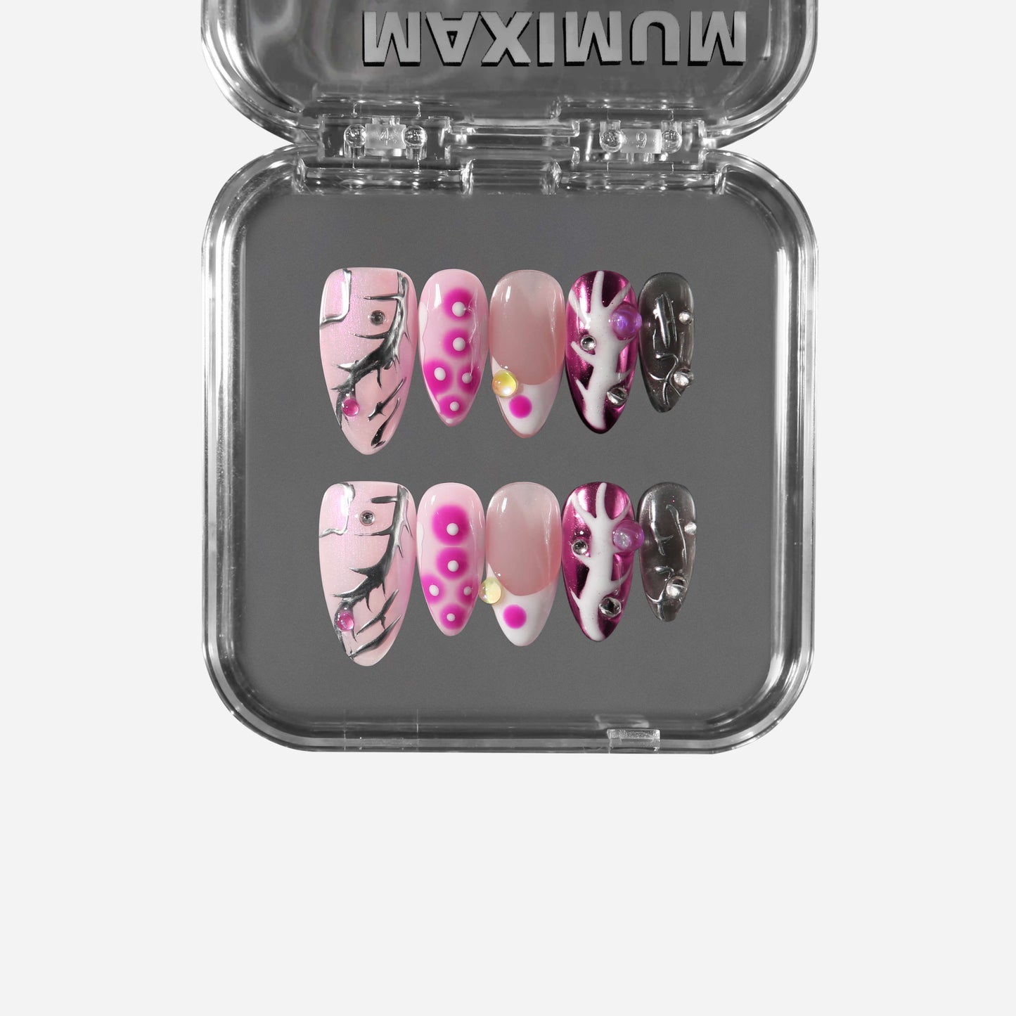 Almond pink press-on nails with chrome accents, pearls, studs, hot-pink dots, and black crackle lines for a cyber-coquette aesthetic.