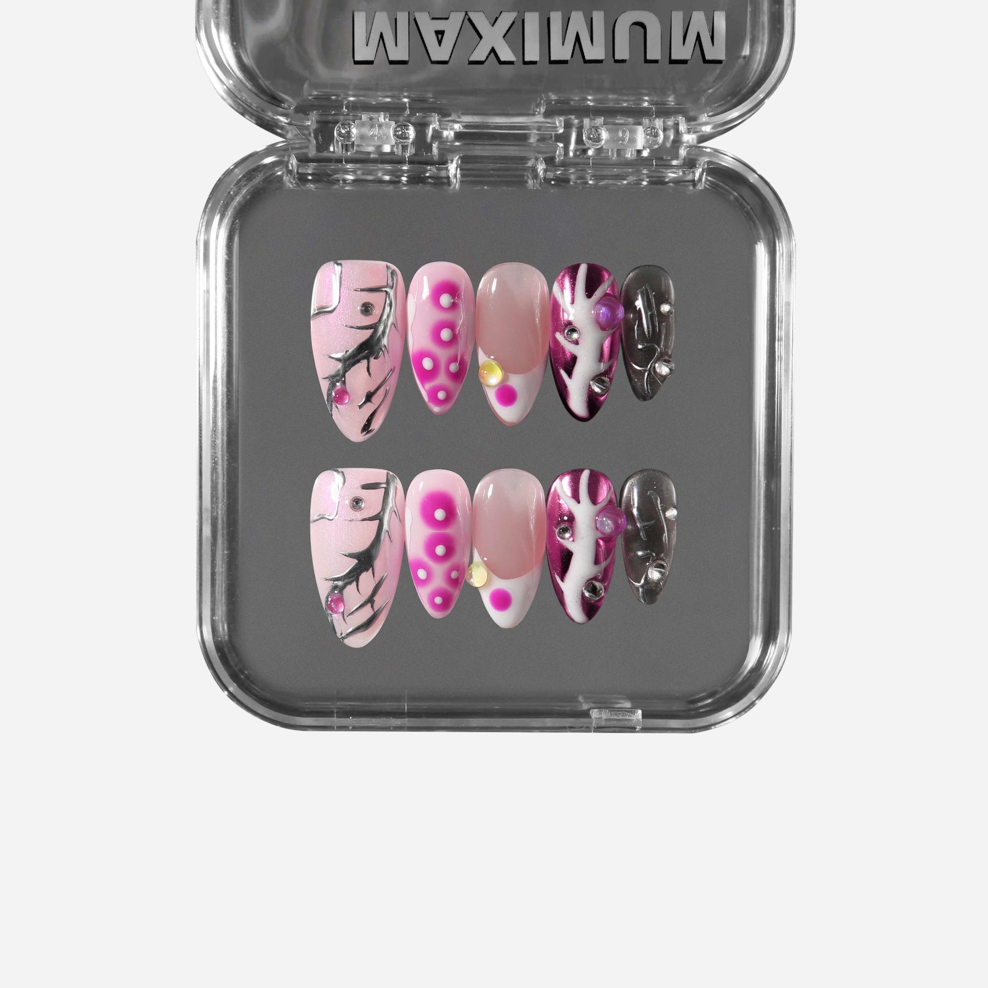 Almond pink press-on nails with chrome accents, pearls, studs, hot-pink dots, and black crackle lines for a cyber-coquette aesthetic.