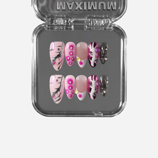 Almond pink press-on nails with chrome accents, pearls, studs, hot-pink dots, and black crackle lines for a cyber-coquette aesthetic.