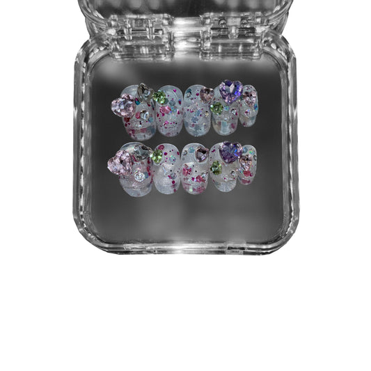 "Gemborn" – a short round press-on nail set featuring a translucent base, sparkling glitter, and 3D gemstone embellishments in dreamy pastel hues.