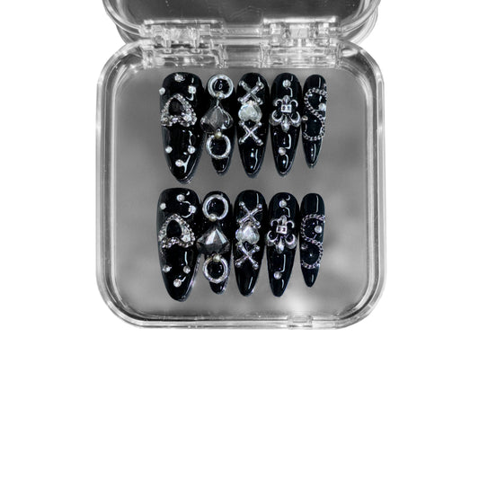 Gutter Saint – a black stiletto press-on nail set featuring punk-inspired chain details, metallic embellishments, and gothic symbols for a rebellious statement look.