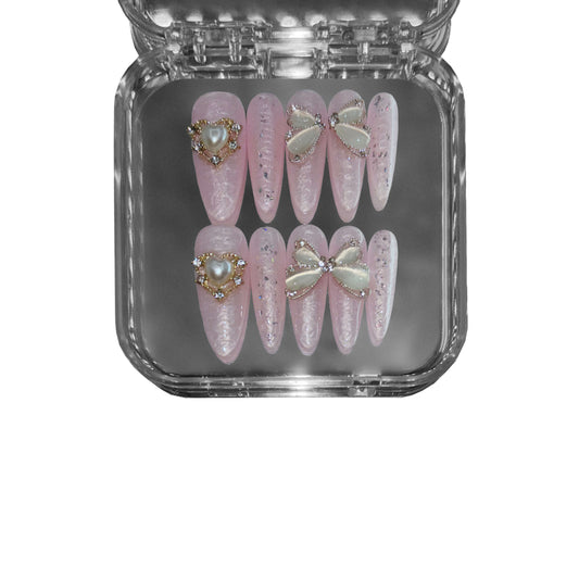 "Oyster Blush" – a pink stiletto-shaped press-on nail set featuring an iridescent pearl sheen, 3D rippled texture, and delicate butterfly wing embellishments for a refined aesthetic.